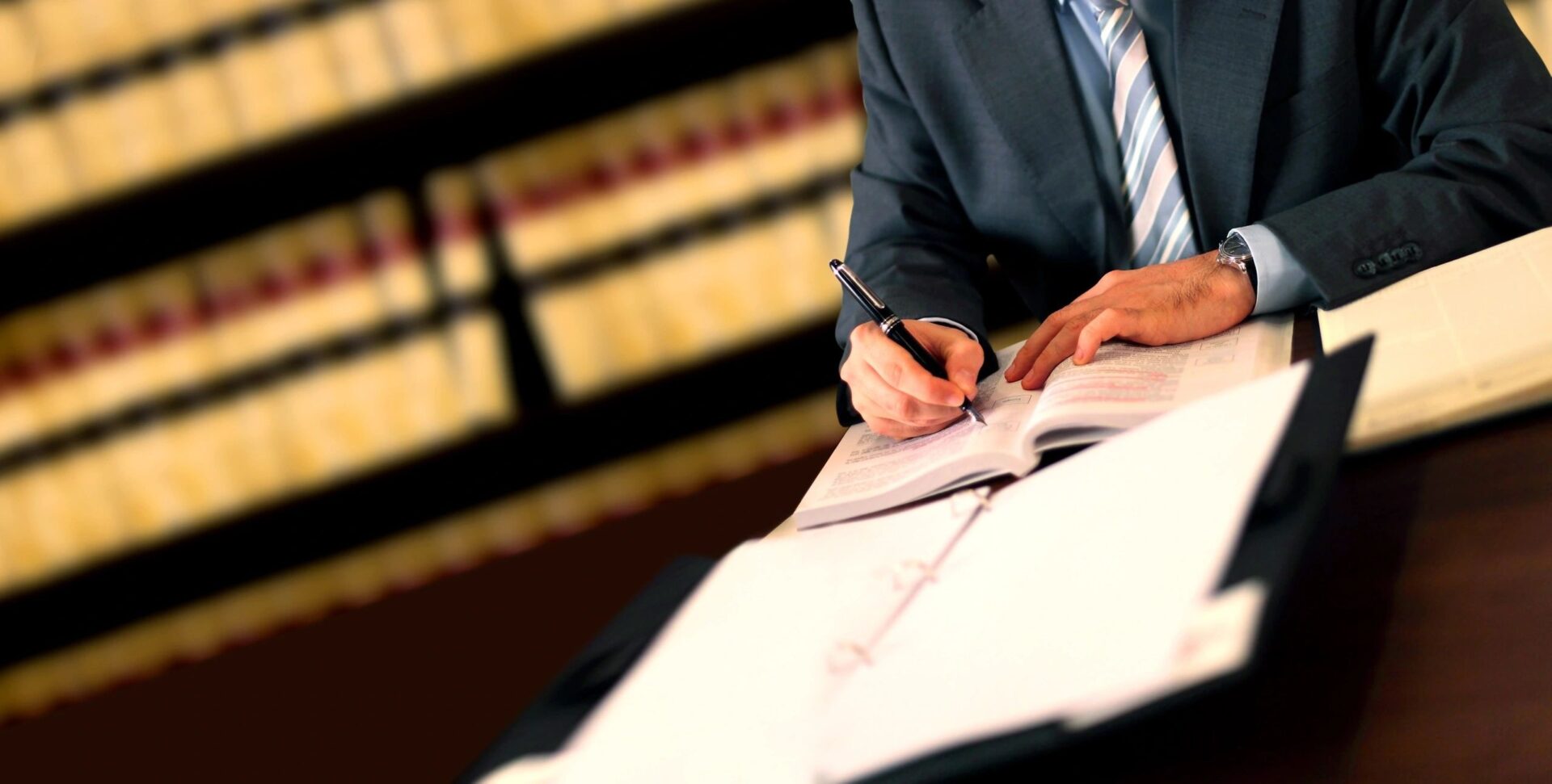 A person in suit writing on paper near book.