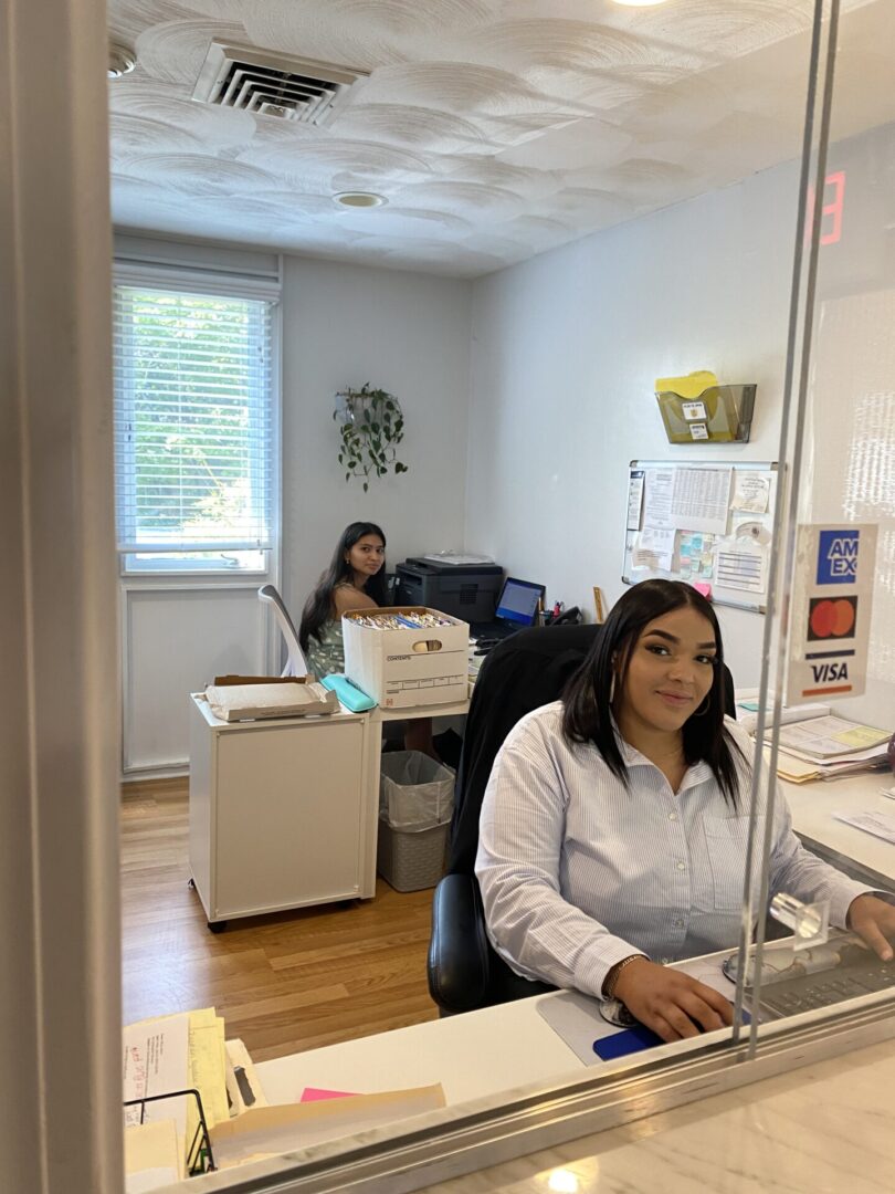 Two women are sitting at a desk in an office.